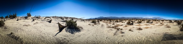 The image depicts a panoramic view of a desert landscape under a clear blue sky. The foreground features a sandy terrain with sparse vegetation, including small bushes and shrubs scattered across the ground. The sand appears light-colored, with ripples and patterns created by wind erosion. In the midground, several triangular-shaped objects, possibly hammocks or tarps, are visible, adding a human element to the otherwise natural scene. The background showcases a range of mountains with snow-capped peaks, indicating a high elevation. The sky is a deep blue, with no visible clouds, suggesting a dry and arid climate. The overall composition emphasizes the vastness and isolation of the desert environment.</p>

<p>Provided by @altbot, generated privately and locally using Ovis2-8B
