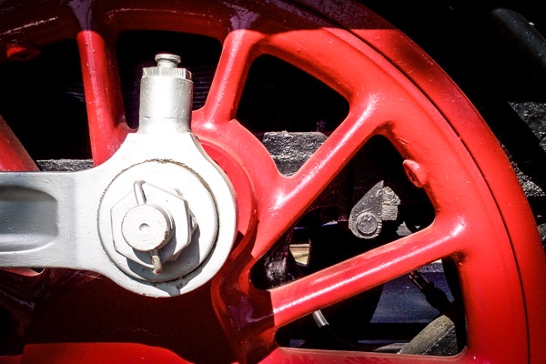 The image shows a close-up view of a red wheel, likely part of a locomotive or industrial machinery. The wheel has a bright red color with a glossy finish, and its spokes are visible, radiating from the center. The central hub is silver and features a large bolt, which is likely used to secure the wheel to the axle. The bolt is surrounded by a white metal arm, which connects the wheel to the rest of the machinery. The background is dark, providing contrast to the red wheel and highlighting its details. The wheel's spokes are evenly spaced, and the overall structure appears robust and well-maintained.</p>

<p>Provided by @altbot, generated privately and locally using Ovis2-8B