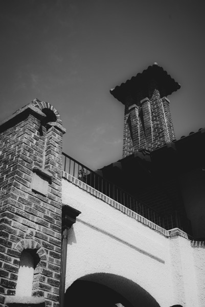  The image is a black and white photograph of a building with a prominent brick tower. The tower features a square base with a tiled roof and is constructed from dark bricks, with visible mortar lines. The building has a white stucco facade with a smooth texture, contrasting with the rough brickwork. An arched opening is visible at the base of the tower, and a small arched niche is present on the brick wall. A black metal railing runs along the top of the building, and a clear sky is visible in the background. The image is taken from a low angle, emphasizing the height of the tower and the architectural details.</p>

<p>Provided by @altbot, generated privately and locally using Ovis2-8B