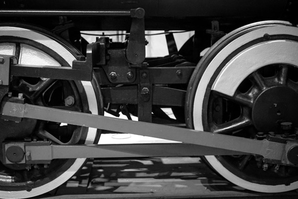 The image is a black and white photograph of a section of a train's undercarriage, focusing on the wheels and connecting rods. The photograph captures the intricate details of the mechanical components, including two large wheels with white rims and black spokes. The wheels are connected by a metal rod, which is part of the train's drive mechanism. The background is blurred, emphasizing the wheels and rods in the foreground. The image highlights the textures and materials used in the construction of the train, showcasing the engineering and craftsmanship involved in its design.</p></p>

<p><p>Provided by @altbot, generated privately and locally using Ovis2-8B
