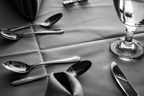 The image depicts a table setting in black and white. The table is covered with a smooth, dark-colored tablecloth. In the foreground, there are three shiny silver spoons arranged parallel to each other, with their handles pointing towards the bottom right corner of the image. A neatly folded napkin is placed to the left of the spoons, partially overlapping them. To the right, there is a clear wine glass with a stem, filled with a clear liquid, possibly water. A butter knife with a polished blade is positioned diagonally, with its handle pointing towards the bottom right corner. The overall composition is clean and orderly, with the utensils and glass arranged symmetrically on the table.</p></p></p></p>

<p><p><p><p>Provided by @altbot, generated privately and locally using Ovis2-8B