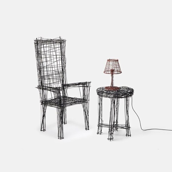 The image features a high-back chair and a small round table, both constructed from black wire. The chair has a tall backrest and armrests, with a seat made of intersecting wire strands. The table has a round top and three legs, also made of wire. A small lamp with a wireframe shade sits on the table, connected by a black cord. The background is plain white, emphasizing the wire structures. The overall design is minimalist and artistic, with a focus on the interplay of lines and shapes.</p>

<p>Provided by @altbot, generated privately and locally using Ovis2-8B